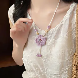 Close-up of a handmade woven purple flower necklace with beads on a model.