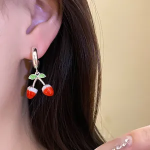 Detalle de pendientes de aro plateados con colgantes de fresa roja en una oreja real