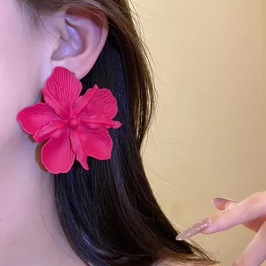 Close-up of large matte magenta flower stud earrings on ear for a tropical vacation style.