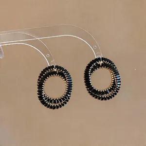 Detailed view of oval interlocking stud earrings with black baguette stones in gold finish
