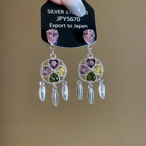 Close-up of vintage flower drop earrings with colorful heart zircons and feather tassels.