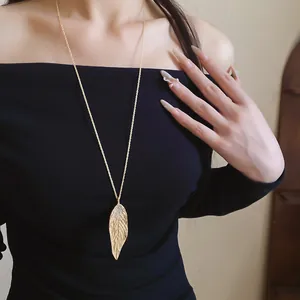 Detailed view of an elegant gold leaf pendant necklace on a long chain worn by model