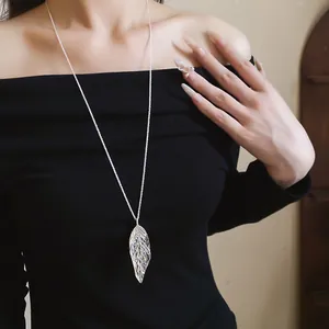 Close-up of a silver leaf pendant necklace worn on an elegant black off-shoulder top