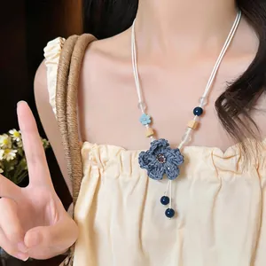 Close-up of a woven blue flower necklace with wooden and ceramic beads on a model.