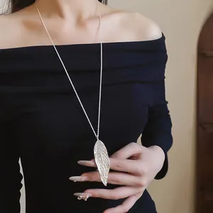 Close-up of large textured silver leaf pendant on a long chain worn by a model.