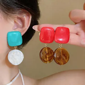 Detail view showing geometric resin earrings in vibrant teal, white, red, and amber shades