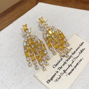 Dettaglio di orecchini a perno in argento con nappe di zircone giallo e pietre quadrate.