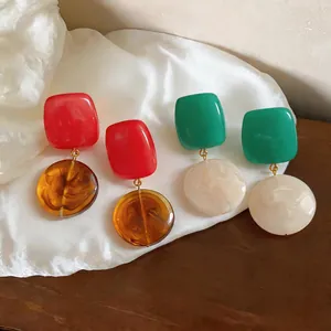 Macro view of geometric resin earrings showing marbled textures in red, green and amber
