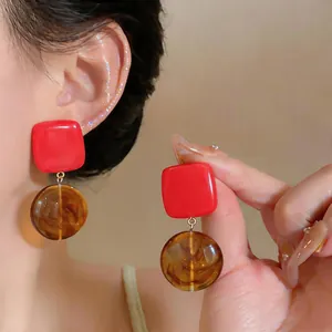Close-up of red and brown resin geometric earrings worn on ear and held by hand