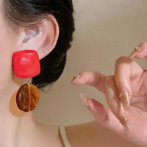 Detailed macro view of red and amber resin geometric drop earrings worn on a model's ear