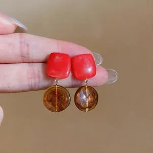 Macro detail view of geometric resin earrings featuring red square and amber round elements