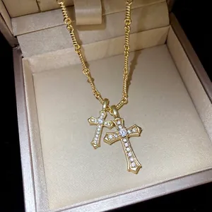 Elegant gold double cross pendant necklace with shimmering zircons in a beige jewelry box