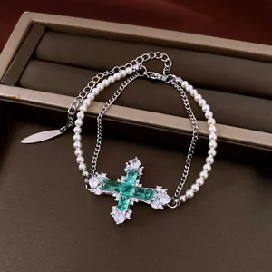 Detailed view of a double-layer pearl and chain bracelet with a green cross pendant.