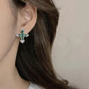 Macro view of a vintage cross stud earring with emerald-green and clear zircon stones.