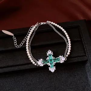 Detailed view of a double-layered pearl and zircon bracelet with a green cross pendant