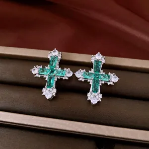 Close-up of luxury cross stud earrings with emerald-green and clear zircon stones