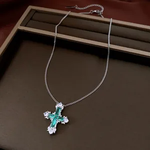 Detailed view of a silver-toned necklace with an emerald green and white zirconia cross pendant