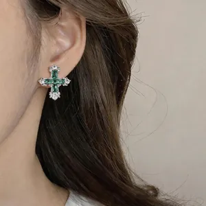 Detail view of vintage emerald green cross stud earrings with zircon stones on a model