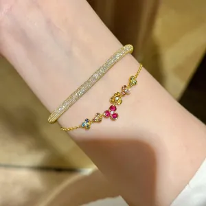 Gros plan d'un bracelet en or avec des breloques fleurs colorées et un jonc assorti.