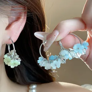 Dettaglio di orecchini a cerchio con fiori in resina nei toni del blu e del verde tenue