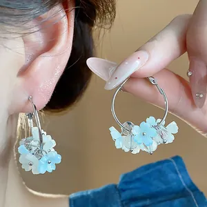 Primo piano di orecchini a cerchio con fiori in resina blu e bianchi indossati da modella