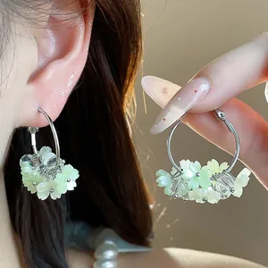 Dettaglio di orecchini a cerchio con fiori in resina verde indossati e tenuti in mano.