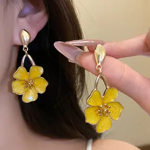 Close-up detail of vintage yellow enamel flower drop earrings featuring a gold finish