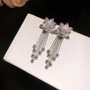 Detailed view of silver flower earrings with zircon center and dangling bead tassels