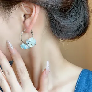 Dettaglio ravvicinato di orecchini a cerchio con fiori in resina azzurra su modella