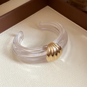 Makroaufnahme eines minimalistischen klaren Harz-Armreifs mit einem goldenen Muschel-Detail.