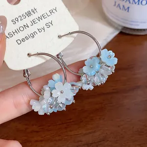 Dettaglio di orecchini a cerchio in argento decorati con fiori di resina bianchi e blu