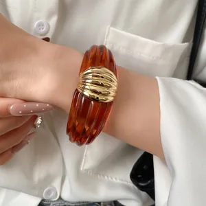 Detailansicht eines breiten Armreifs aus bernsteinfarbenem Harz mit goldenem Mittelstück