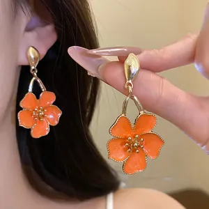 Close-up of elegant orange flower pendant earrings with gold edges shown on ear and held