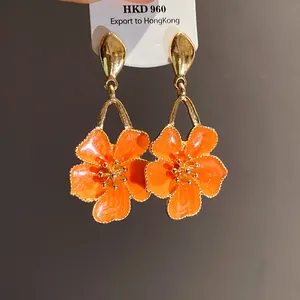 Close-up of elegant orange oil-drop flower pendant earrings with gold-tone finish