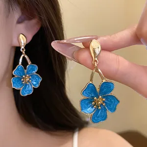 Detailed close-up of blue oil-drop flower earrings with golden finish and petal details.