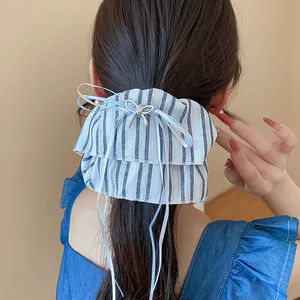 Detail view of a striped fabric scrunchie with a silver metal bow and long ribbons.