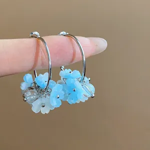 Primo piano di orecchini a cerchio con fiori in resina blu e finitura color argento