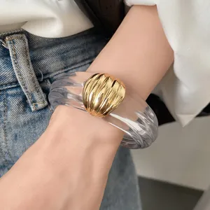 Detailansicht eines transparenten Harzarmreifs mit goldener Muschelverzierung am Handgelenk.