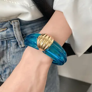 Nahaufnahme eines blauen transparenten Harzarmreifs mit strukturierten Goldmetallelementen.