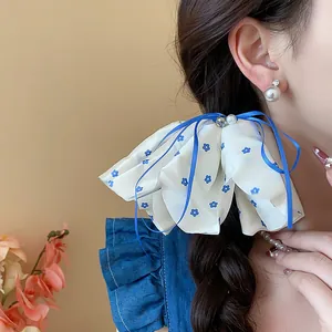Close-up of elegant floral scrunchie with blue ribbons and pearl accents on braided hair.
