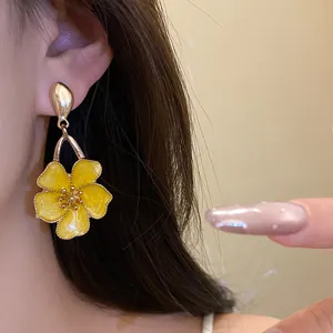 Close-up detail of a vintage yellow enamel flower drop earring worn with a gold finish