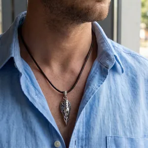 Macro detail of a vintage eagle wing pendant necklace on a brown leather cord for men.