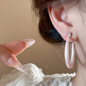 Detalle de elegantes pendientes de botón en forma de C de esmalte rosa con circón.