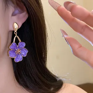 Detail shot of a purple enamel flower pendant earring featuring retro golden hardware on ear