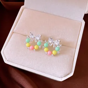 Boucles d'oreilles nœud en zircon avec des perles pastel dans un coffret crème.