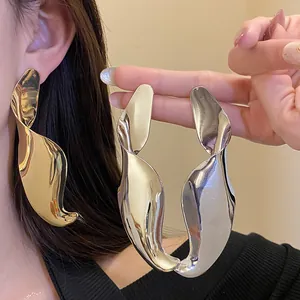 Detailed view of oversized geometric twisted drop earrings in gold and silver finishes.