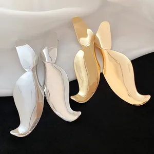Close-up of oversized geometric twisted drop earrings featuring mirror finish in gold and silver