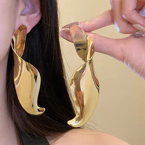 Detailed view of oversized gold geometric twisted statement drop earrings on model.