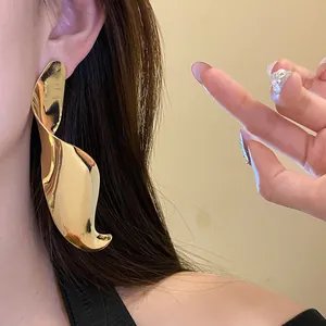 Macro detail of high-shine gold geometric twisted pendant earring worn by Asian model