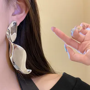 Detailed macro view of oversized silver geometric twisted drop earrings on model's ear